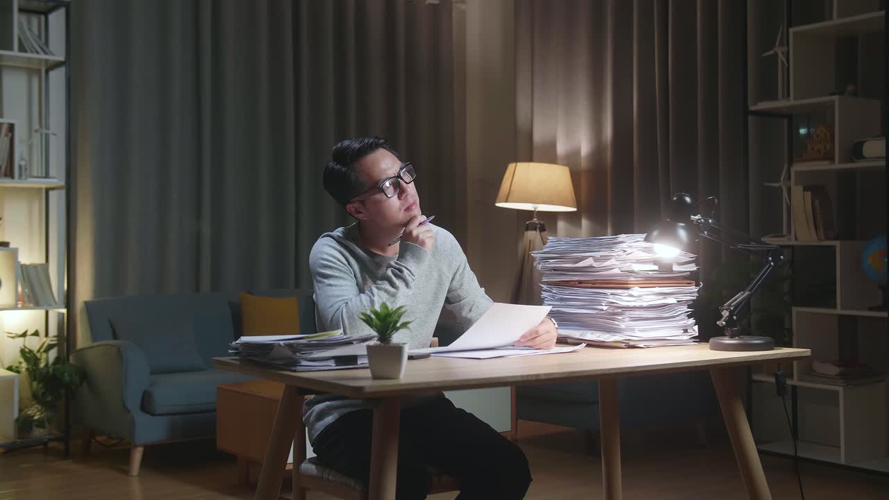 Asian Man Thinking And Looking At Paper Then Raising Index Finger While Working With Documents At Home