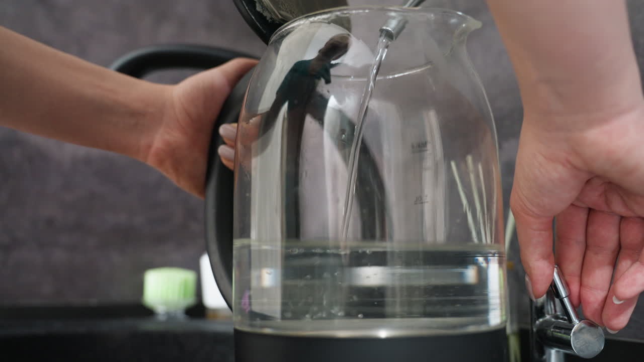 Vorbereitung des Kessels für den Kochvorgang, moderne Küchenszene mit Kesseln, die zum Kochen bereit sind, Person, die einen transparenten elektrischen Kessel auf einer Basis in einer modernen Küche anordnet, um den Kochvorgang zu beginnen