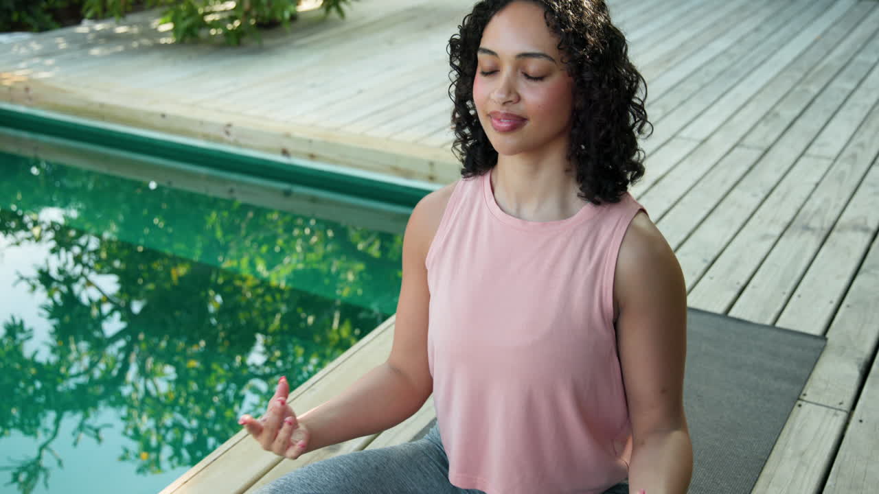 Meditating by pool, woman in pink top enjoying peaceful outdoor moment