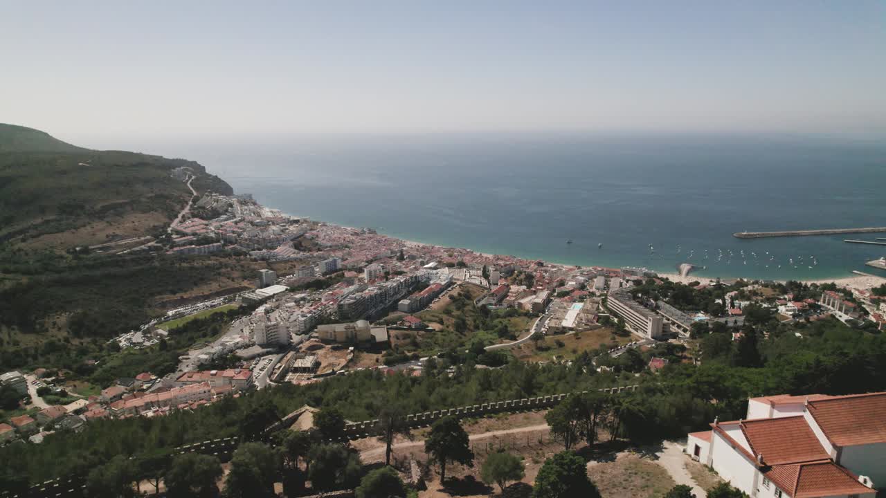 antena hacia atrás sobre los muros del castillo y la iglesia de santa maria do castelo con la ciudad de sesimbra y el paisaje marino en el fondo, portugal