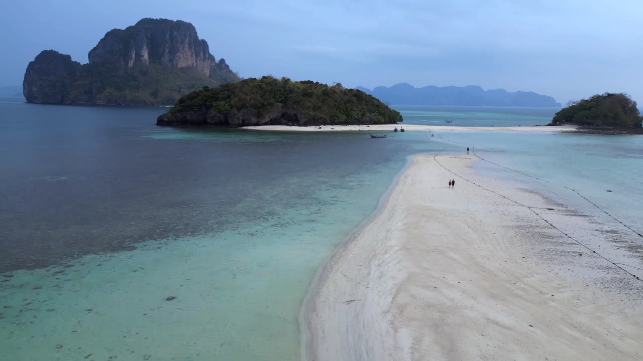 couple lonely on a sandbank at Ko Kai island with turquoise tropical sea and boat, Krabi, Thailand. Tremendous aerial view flight descending drone