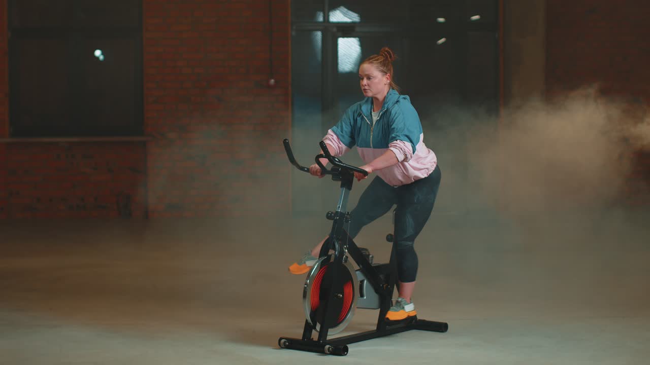 Healthy caucasian woman exercising workout on stationary cycling machine bike in gym slow motion