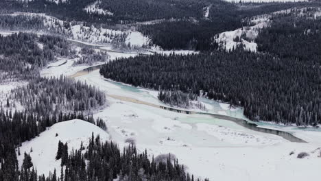 the takhini river, encircled by a snowy, dense forest during winter in yukon, canada - orbit drone shot