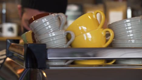 tazas limpias para café en la parte superior de la máquina de espresso inoxidable con barista masculino enmascarado detrás