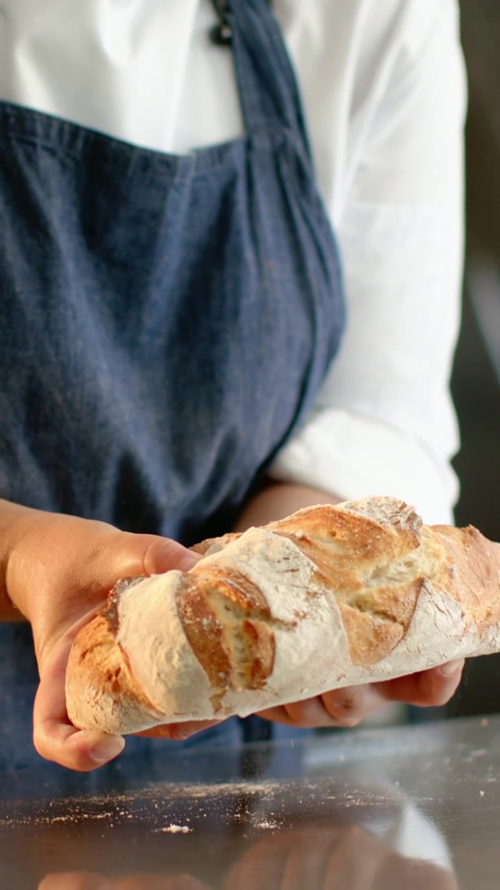 Vertical video: Lifting chef in jacket and apron turning floured loaf on steel counter for display