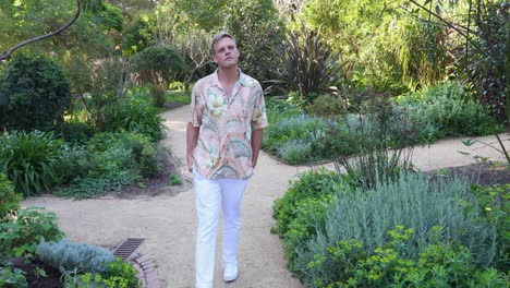 Young-male-in-hawain-shirt-walks-through-wooden-archway-in-garden_slow-motion-1