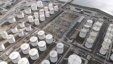 top-down aerial of symmetrical riverside fuel tank farm with white cylinders, yellow railings, catwalks and pipelines conveying large-scale petrochemical storage operations