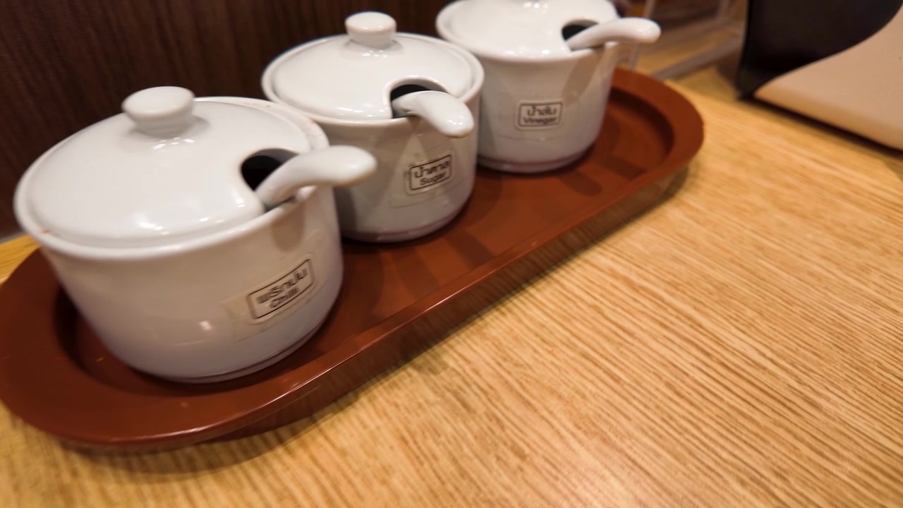 Close-up zoom out of white ceramic condiment jars on a wooden tray in Bangkok.