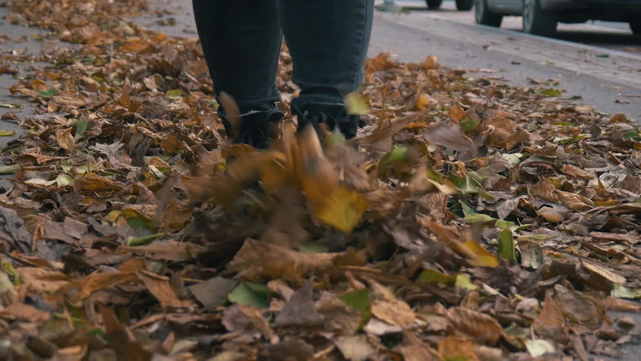 Girl walking and kicking fall yellow and orange dusty leaves slow motion front shot