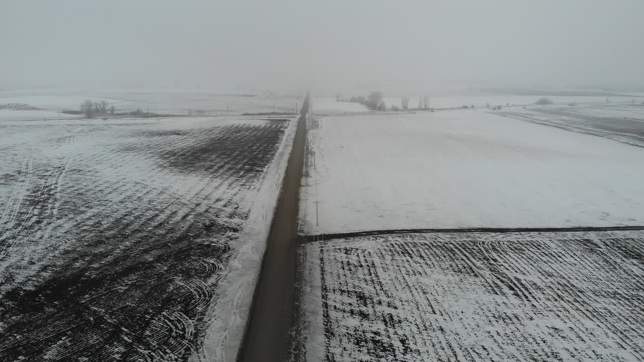 겨울에 눈이 내리는 빈 흙길을 가로질러 움직이는 무인 항공기 공중 샷