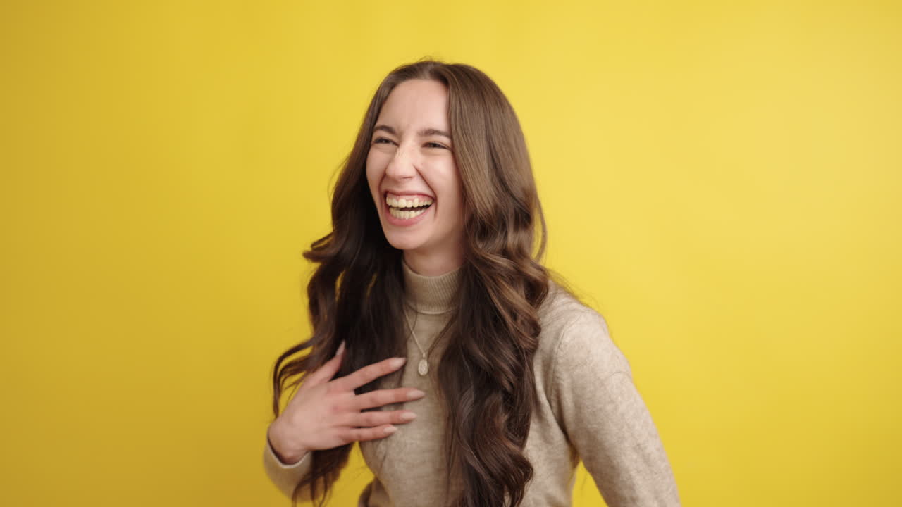 Young woman laughing on yellow background