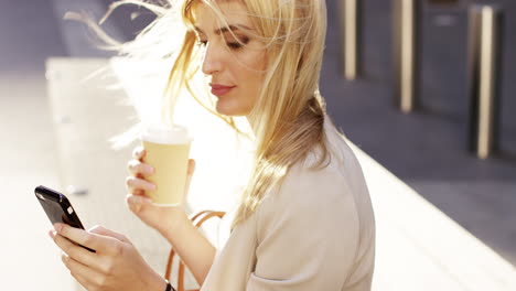 attractive blonde business woman using smartphone drinking coffee commuter in city london