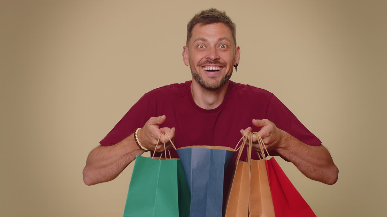un joven feliz y sonriente mostrando bolsas de compras, descuentos publicitarios, asombrado por los precios bajos