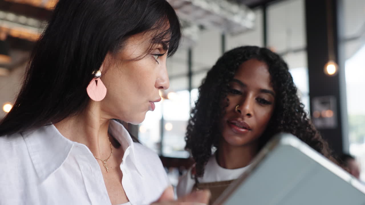 Two Women Discussing Business on a Tablet in a Cafe