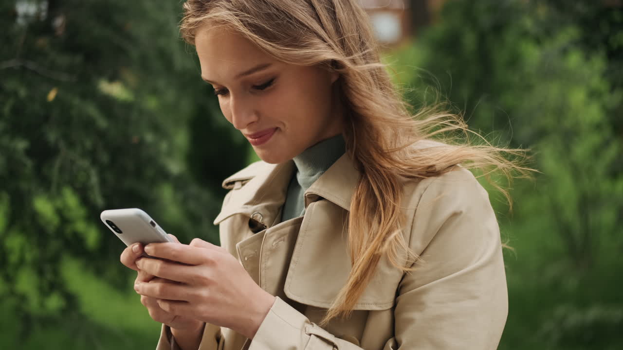 Happy Caucasian female student using smartphone outdoors.