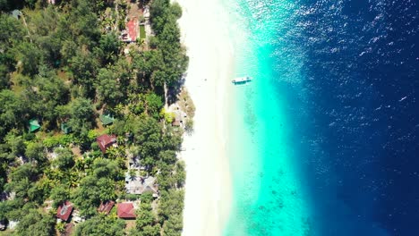 Tranquil-tourist-village-with-houses-under-tropical-trees,-in-front-of-white-sand-of-exotic-beach-and-blue-azure-crystal-sea-in-Bali