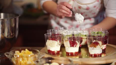 woman preparing layered dessert cups in a kitchen