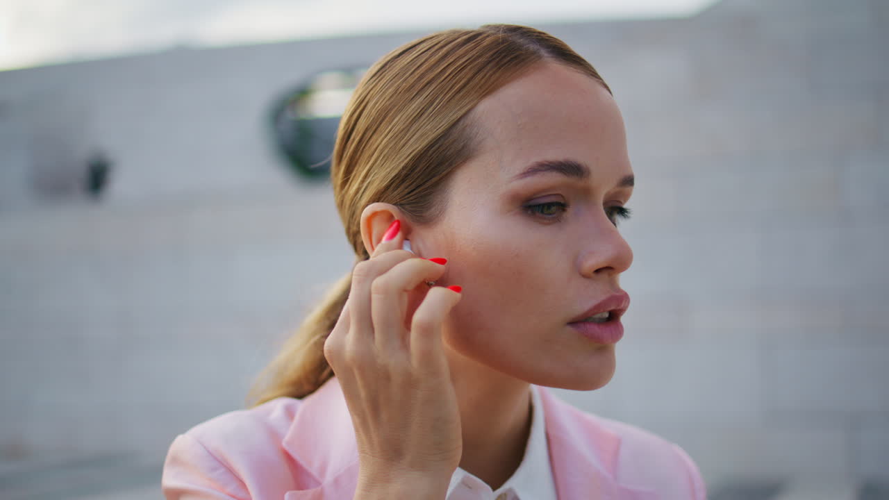 mujer de negocios poniendo auriculares inalámbricos sentada al aire libre en primer plano. mujer elegante