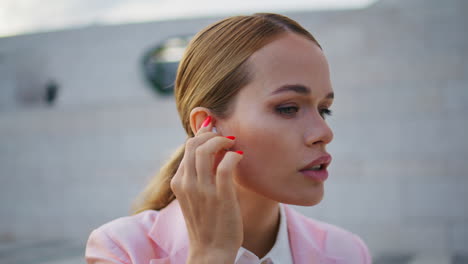 mujer de negocios poniendo auriculares inalámbricos sentada al aire libre en primer plano. mujer elegante