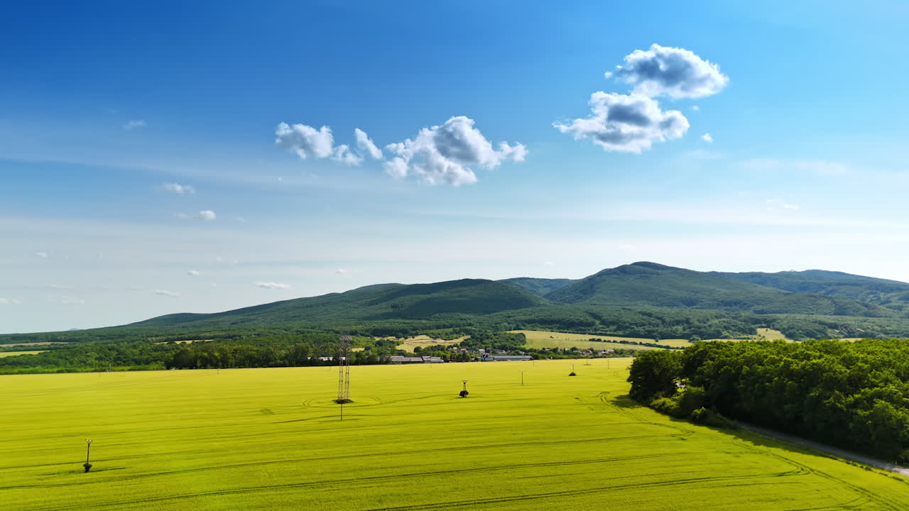 Green fields, blue sky. Bright green fields stretch out towards distant mountains on a clear day with fluffy white clouds above