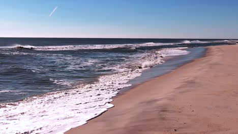 Ein-Niedriger-Blickwinkel-Auf-Einen-Großen-Schwarm-Strandläufer,-Der-An-Einem-Sonnigen-Tag-über-Einen-Leeren-Strand-Fliegt