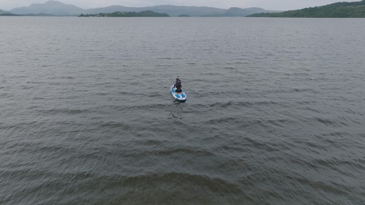 foto de seguimiento de una mujer joven haciendo paddleboarding en loch lomond