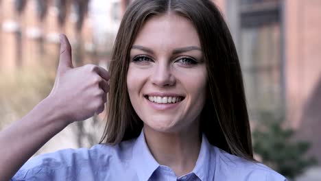 thumbs up by young woman at work,  looking at camera