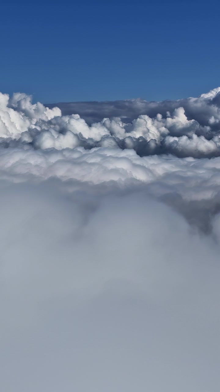 Vertical aerial zoom in through a vast sea of clouds under a bright blue sky.