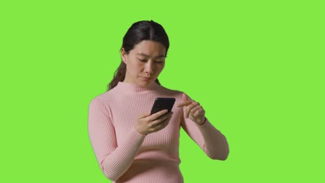 studio shot of woman scrolling through messages or content on mobile phone in front of green screen 1