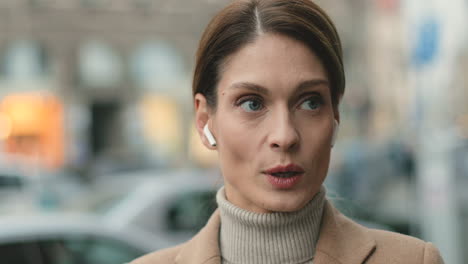 Close-up-view-of-caucasian-businesswoman-wearing-wireless-headphones-while-talking-on-the-phone-in-the-street-in-autumn