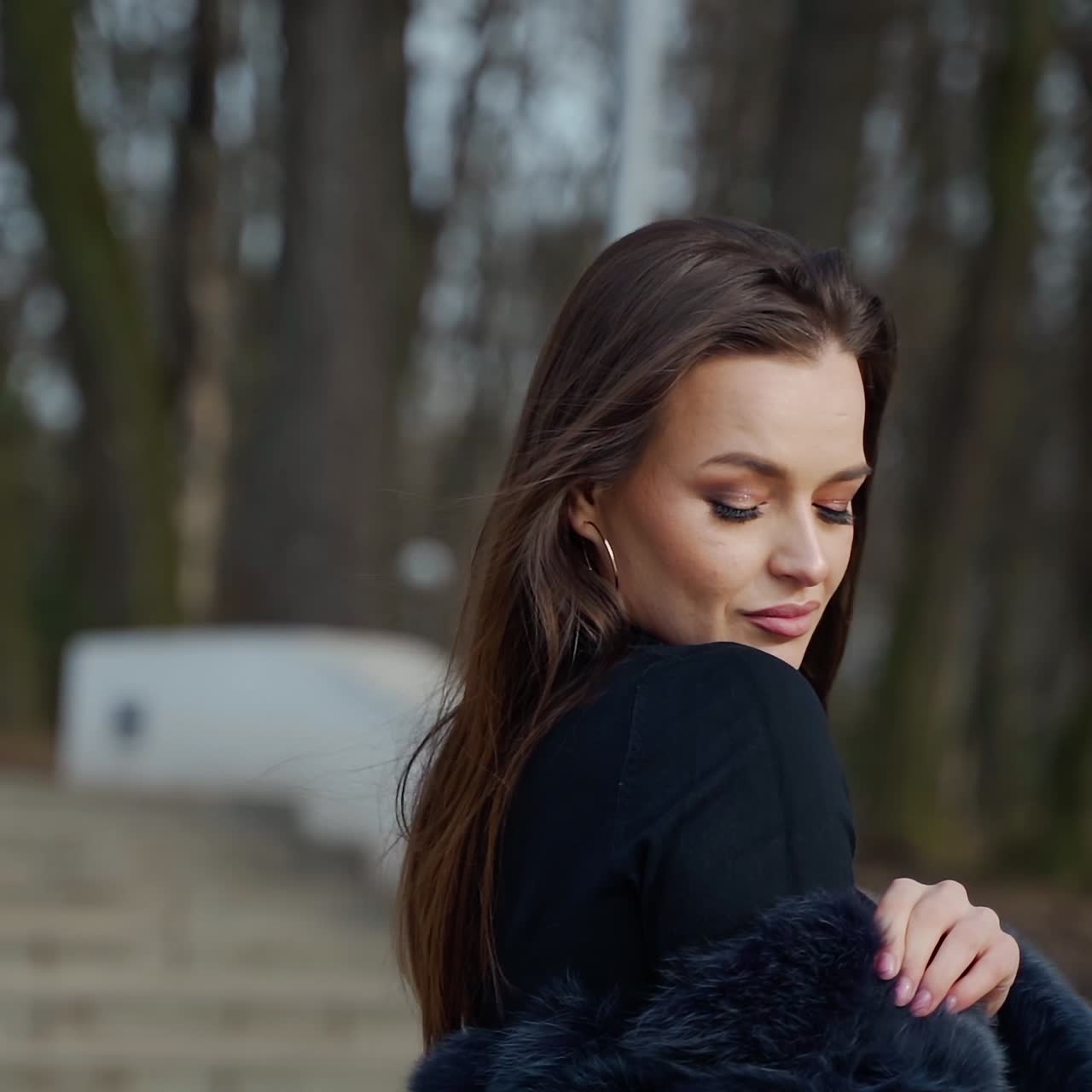 Portrait of beautiful model. Glamour girl in black fur coat posing on camera outdoors. Attractive brunette in the park. Camera moves around.