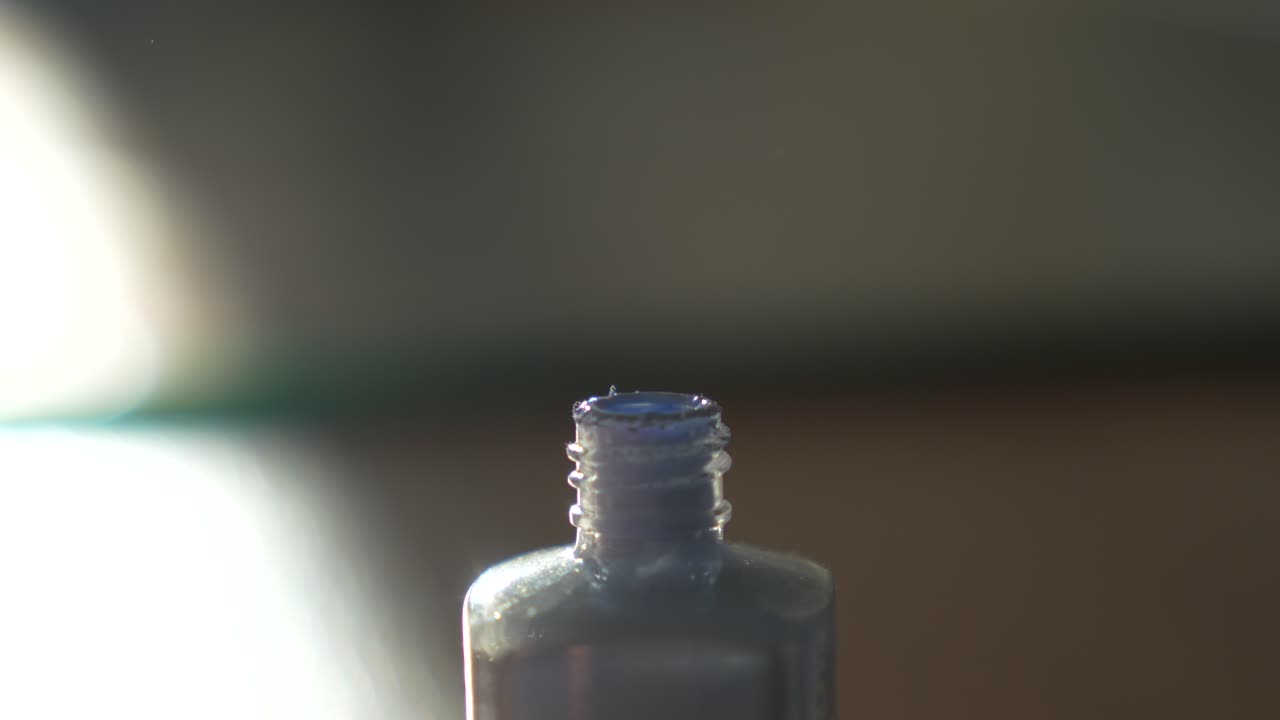 Dipping nail brush in periwinkle polish. Blue cosmetic product bottle