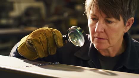 woman inspecting metalwork with magnifying glass