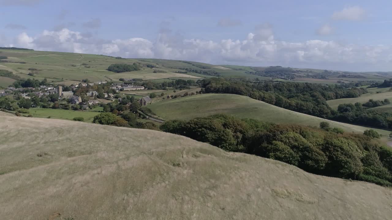 la antena de seguimiento bajo avanza rápidamente por encima de una colina para revelar el pueblo de abbotsbury, en la campiña de dorset