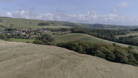 low tracking aerial moves forward fast up above a hill to reveal the village of abbotsbury, in the dorset countryside