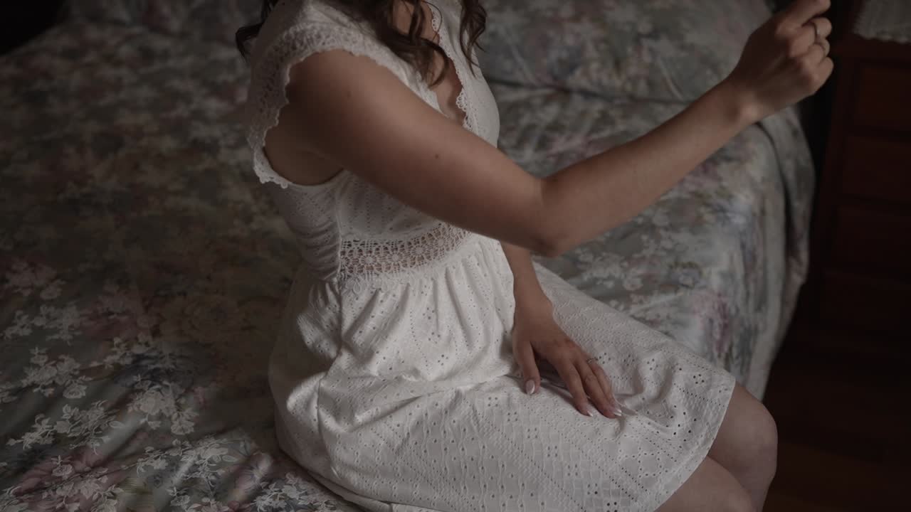 Woman in white lace dress sitting on a floral bedspread in Portugal, calm ambiance