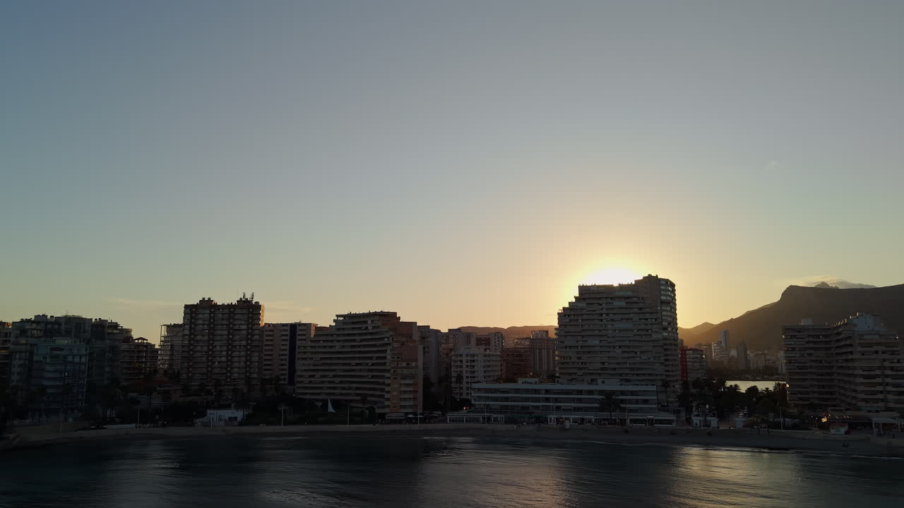 Pôr do sol dourado sobre o horizonte de uma cidade costeira e o oceano.