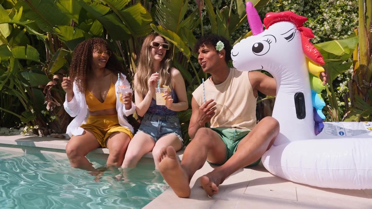 Giovani amici felici che si godono un drink a bordo piscina con un unicorno gonfiabile