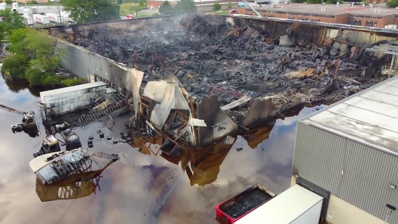 sobrevuelo aéreo de la concha quemada de un almacén industrial con un camión de bomberos a lo largo, toronto