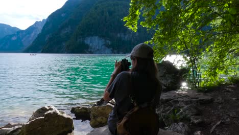 tourist woman adjusting a camera in a pebble beach by the shore of the king's lake, königssee in germany, bavaria