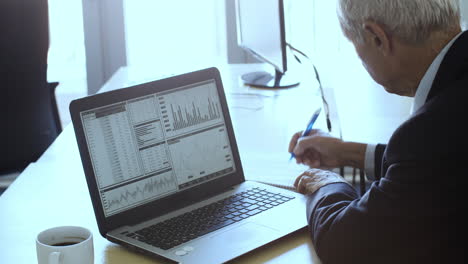 focused mature investor using laptop at workplace