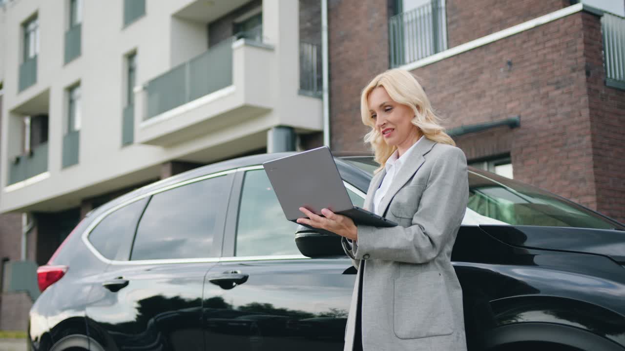 Bella e di successo donna di 40 anni in piedi vicino alla sua auto usa il laptop con interesse e agilità digitando un messaggio all'esterno