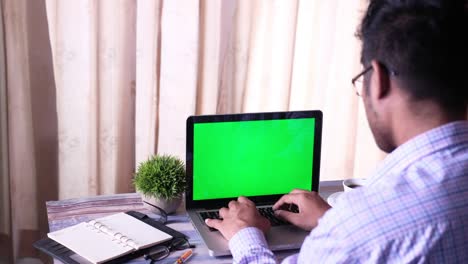 las manos del hombre usando una computadora portátil con pantalla verde en la mesa
