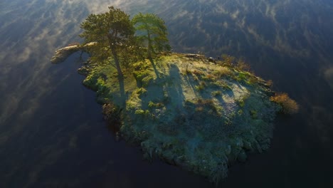 Pequeña-Isla-En-Un-Lago-Tranquilo-Con-Una-Tenue-Niebla-Que-Pasa-Mientras-La-Cámara-Se-Desplaza-Hacia-Abajo