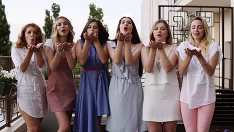 Front-View-Of-Six-Attractive-Young-Women-Playfully-Blowing-Bright-Colored-Confetti-From-Their-Hands-Together