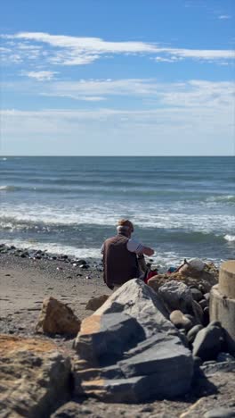 man sitting on a beach watching the waves