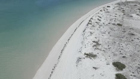 Following-the-coastline-along-the-border-between-the-yellow,-fine-sand-and-the-cold,-blue-sea