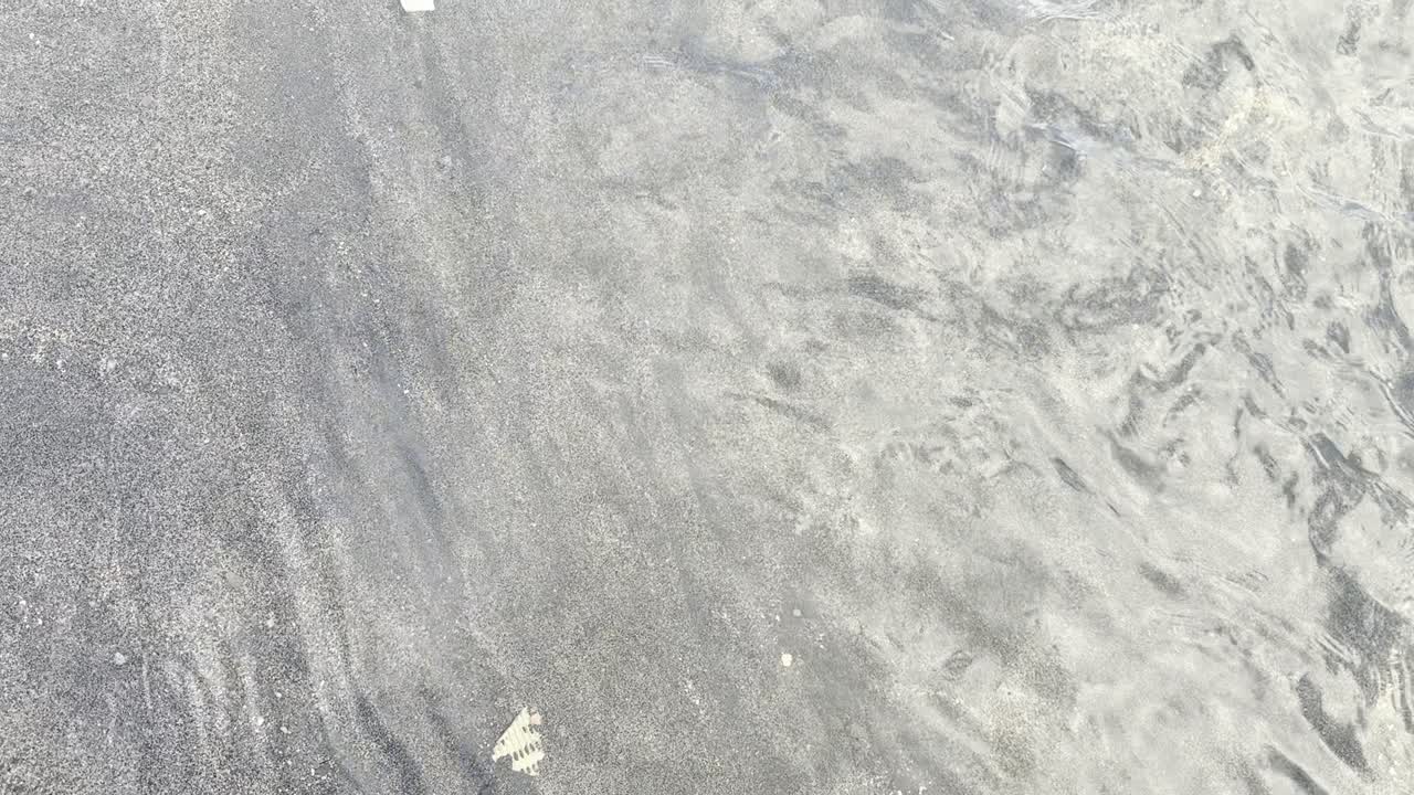 Helder zeewater dat over donker zand stroomt op een strand