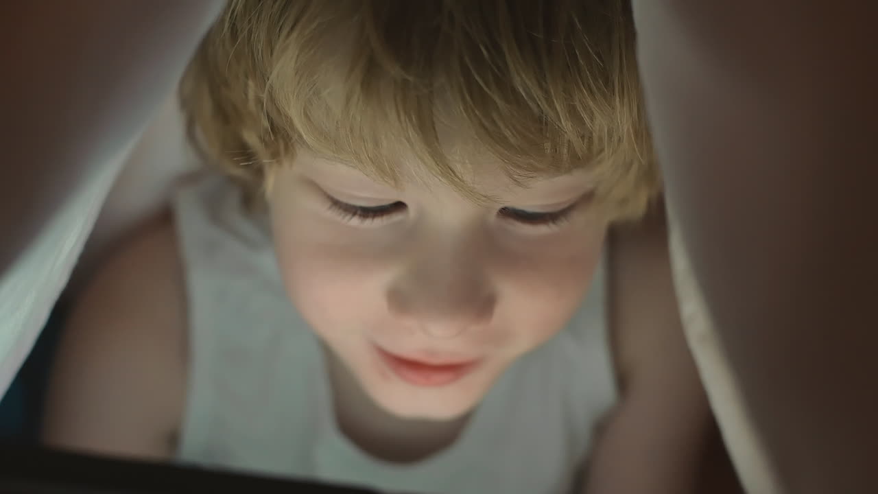 Little Boy Using A Tablet Covered By The Bed Sheet At Night