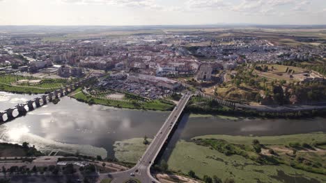 Aerial-view-orbiting-Badajoz-Puente-de-Palmas-bridge-and-Puente-Nuevo-crossing-Guadiana-park-river-towards-bustling-Spanish-city